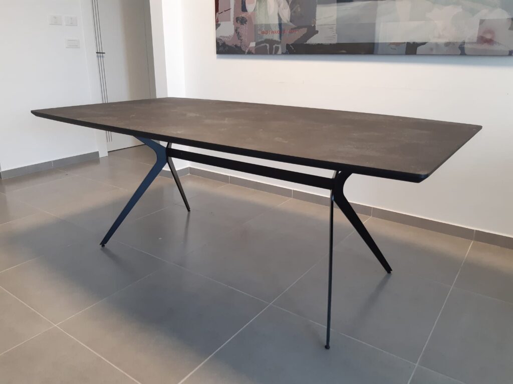 שולחן אוכל מלבני כהה עם רגלי מתכת שחורות מעוצבות על רצפת אריחים אפורה