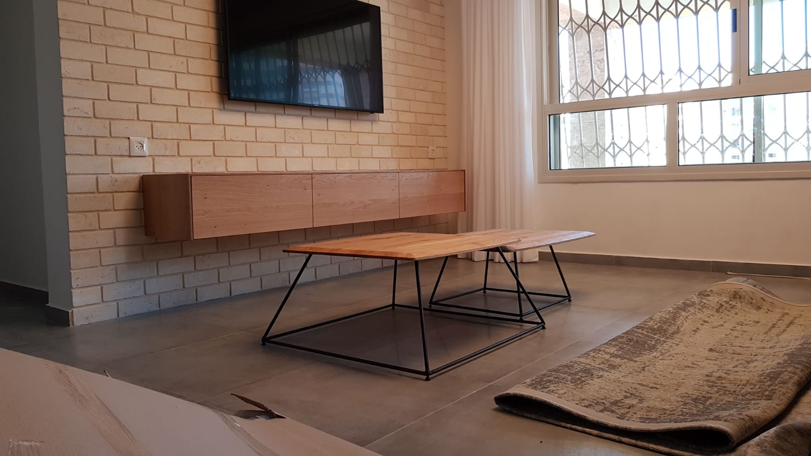 סלון עם קיר לבנים, טלוויזיה, מזנון עץ ושולחנות קפה
