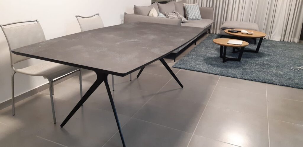 שולחן אוכל אפור כהה עם רגליים שחורות ושני כיסאות בחדר מגורים מודרני.